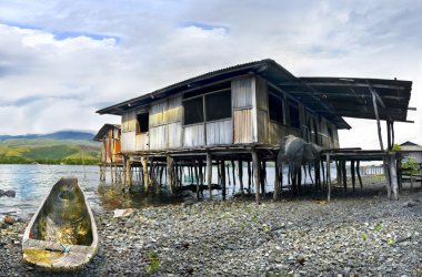 Boat and cottage on piles ashore lake sentani clipart