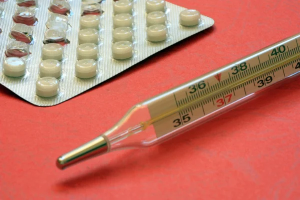Termômetro com pílulas em um fundo vermelho — Fotografia de Stock