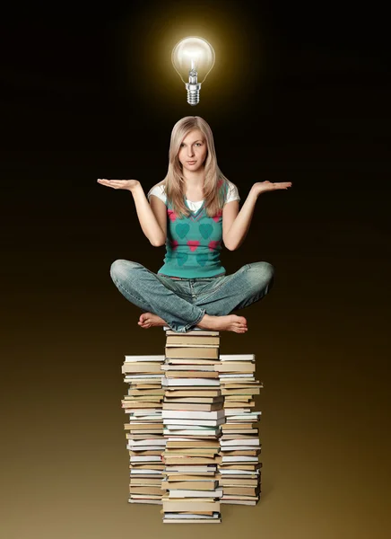 Mujer en la pose de loto equilibrio en la pila de libros y bombilla —  Fotos de Stock