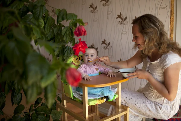 Moeder voeden van hongerige baby in de hoge stoel binnenshuis — Stockfoto
