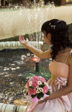 Beautiful bride with flowers near the fountain clipart