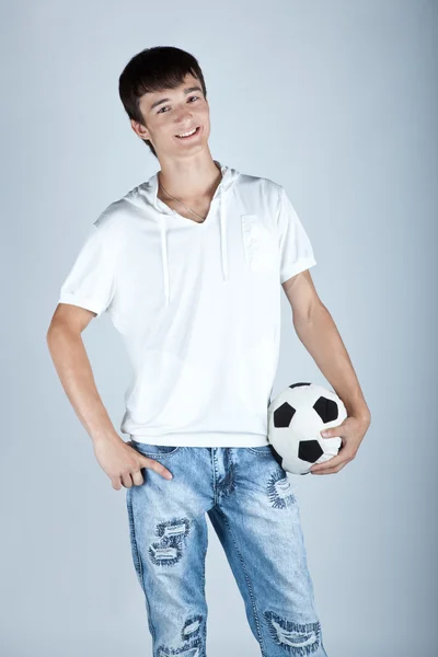 Młody chłopiec trzyma piłkę stopy na białym tle na szarym tle — Zdjęcie stockowe