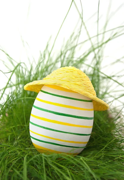 Easter egg in straw yellow hat in green grass — Stock Photo, Image