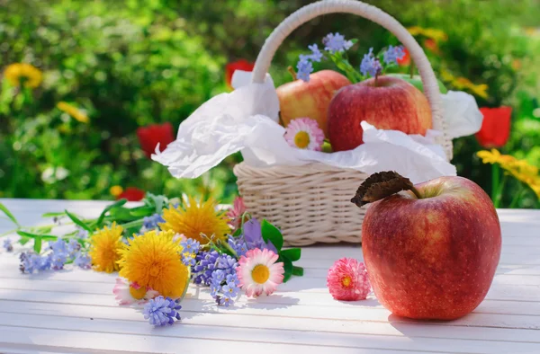 Red apples in basket with flowers in the garden — Stock Photo, Image