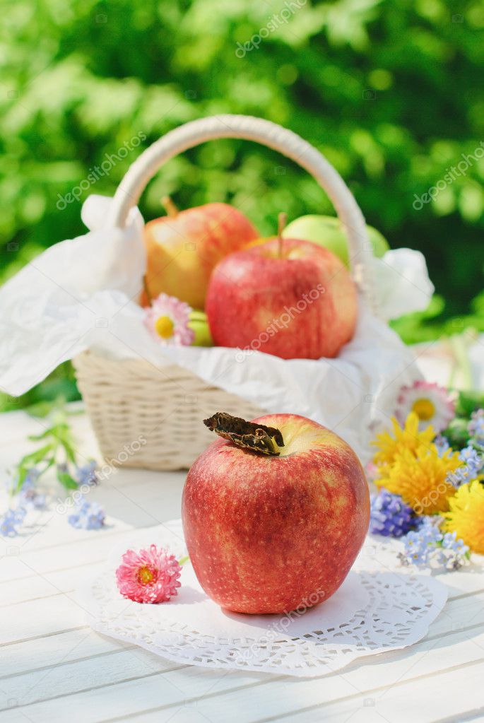 Red apples in the basket with flowers in the garden