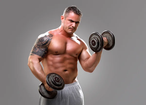 Bodybuilder with a tattoo lifting dumbells, closeup — Stock Photo, Image