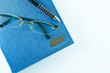 Glasses on blue notebook with black pen in isolation clipart