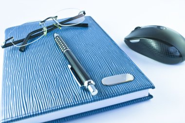 Glasses and black pen on blue notebook with mouse in isolation clipart