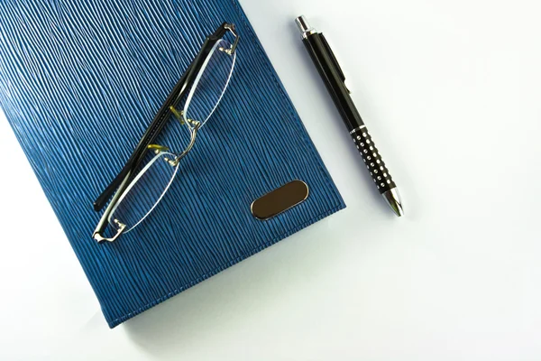 Óculos em caderno azul com caneta preta isolada — Fotografia de Stock