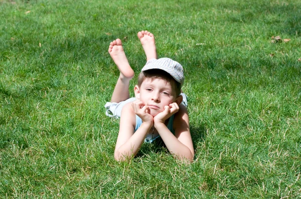 De jongen van vijf jaar legt op een gras — Stockfoto