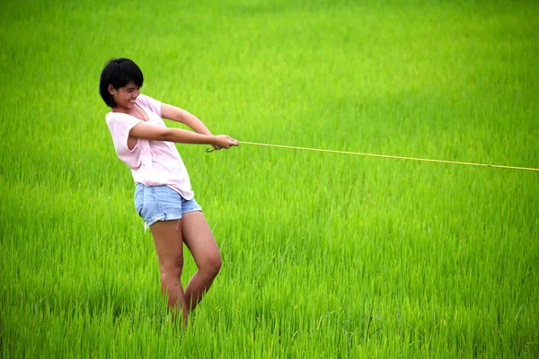 Bezauberndes junges Mädchen zieht gelbes Seil in Reisfeld — Stockfoto