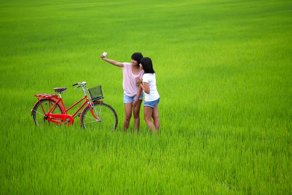 Two girls taking a photo with bike in paddy field — Stock Photo, Image