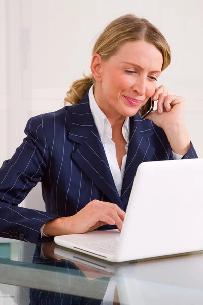 Geschäftsfrau im Büro mit Handy und Laptop — Stockfoto