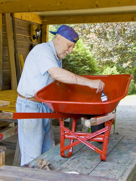 Senior painting a wheelbarrow — Stock Photo, Image