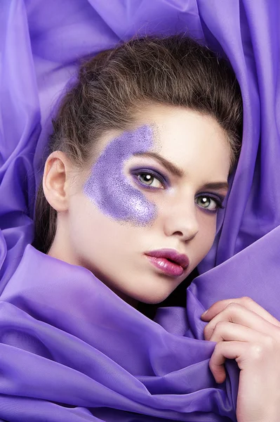 Jeune fille allongée sur du tissu violet portant des paillettes maquillage — Photo