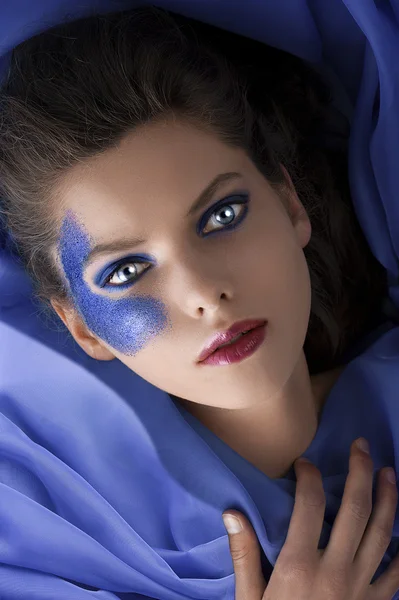 Beautiful girl laying between blue satin sheets — Stock Photo, Image