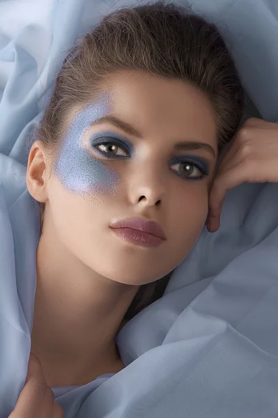 Portrait of a model laying between azure sheets — Stock Photo, Image