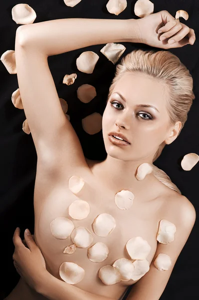 Atemberaubende blonde Mädchen liegt nackt bedeckt mit Rosenblättern — Stockfoto