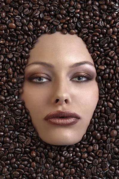 Pretty girl's face immersed in coffee beans — Stock Photo, Image