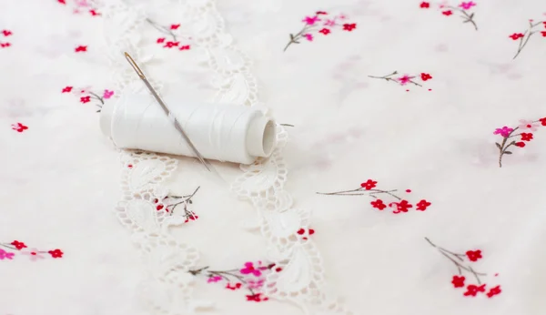 White spool of thread on a floral fabric — Stock Photo, Image