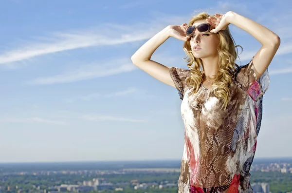 Mooi meisje in zonnebril op achtergrond blauwe hemel — Stockfoto