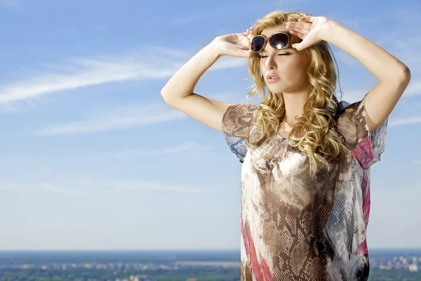 Vacker flicka i solglasögon på bakgrunden blå himmel — Stockfoto