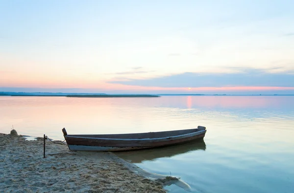 Закат с лодкой у берега летнего озера — стоковое фото