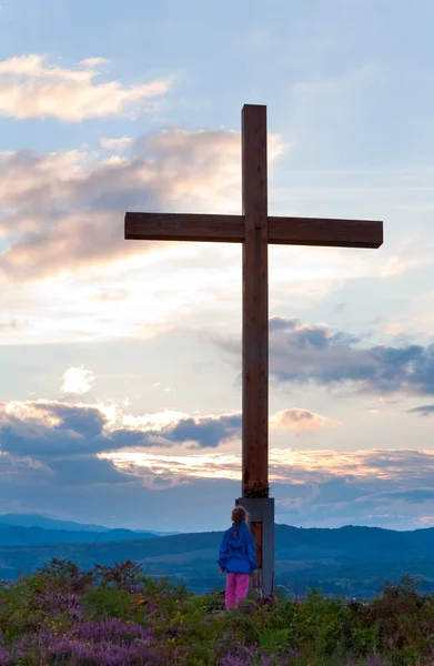 Small girl near wooden cross on summer heather flower hill top — Stock Photo, Image