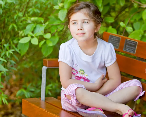 Jong meisje, zittend op een bankje — Stockfoto