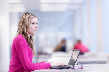 In the library - pretty female student with laptop and books wor clipart