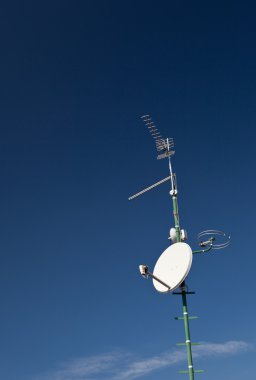 Antennas and a satellite dish on a roof against lovely blue sky clipart