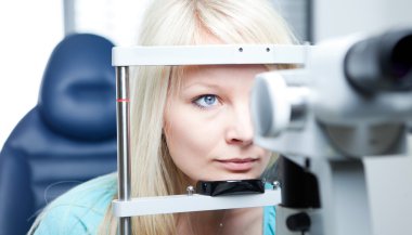 Optometry concept - pretty young woman having her eyes examined clipart