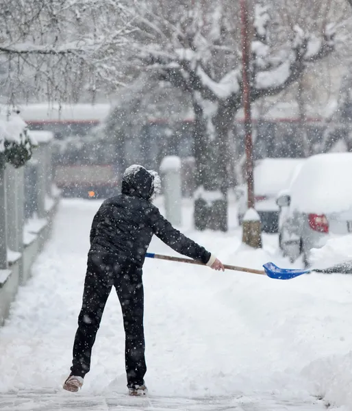 Mujer paleando nieve de una acera después de una fuerte nevada en una —  Fotos de Stock