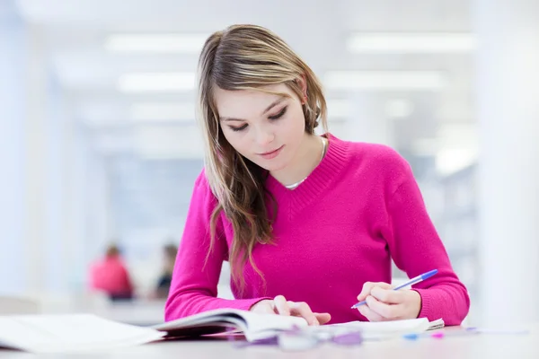 У бібліотеці гарненька студентка з ноутбуком та книжками — стокове фото