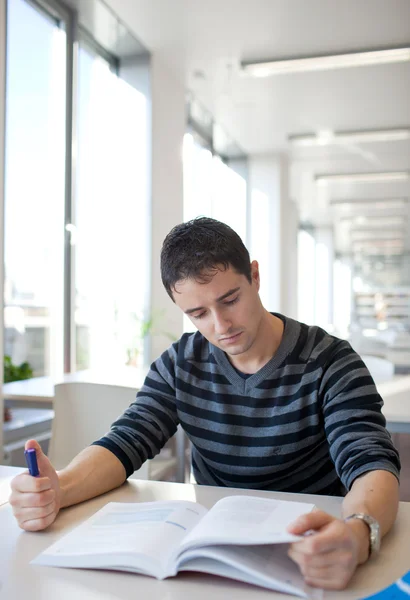 Bonito jovem estudante universitário em uma biblioteca (DOF rasa; cor — Fotografia de Stock