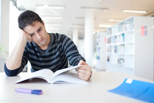 Bonito jovem estudante universitário em uma biblioteca, estudando duro (shal — Fotografia de Stock