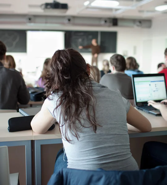 Ung ganska kvinnliga collegestudent sitter i ett klassrum fullt — Stockfoto