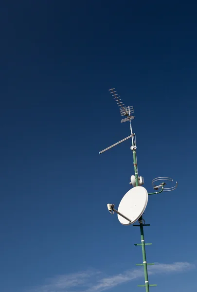 Antenas y una antena parabólica en un techo contra el cielo azul encantador — Foto de Stock