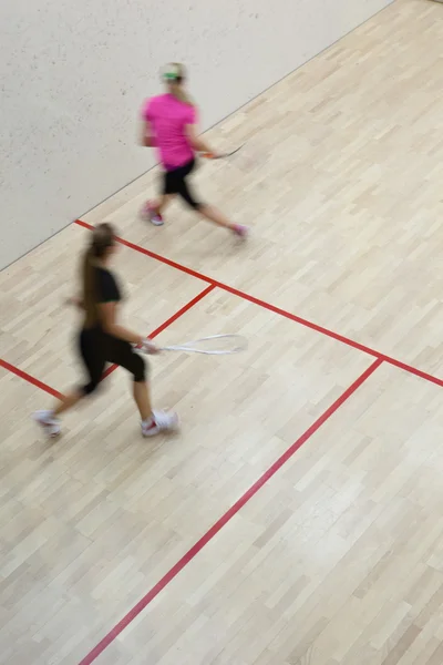 Twee vrouwelijke squash spelers in snelle actie op een squashbaan (moti — Stockfoto