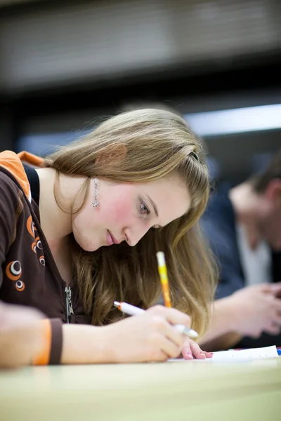 Estudiante universitaria bastante femenina sentado un examen en un salón de clases lleno — Foto de Stock