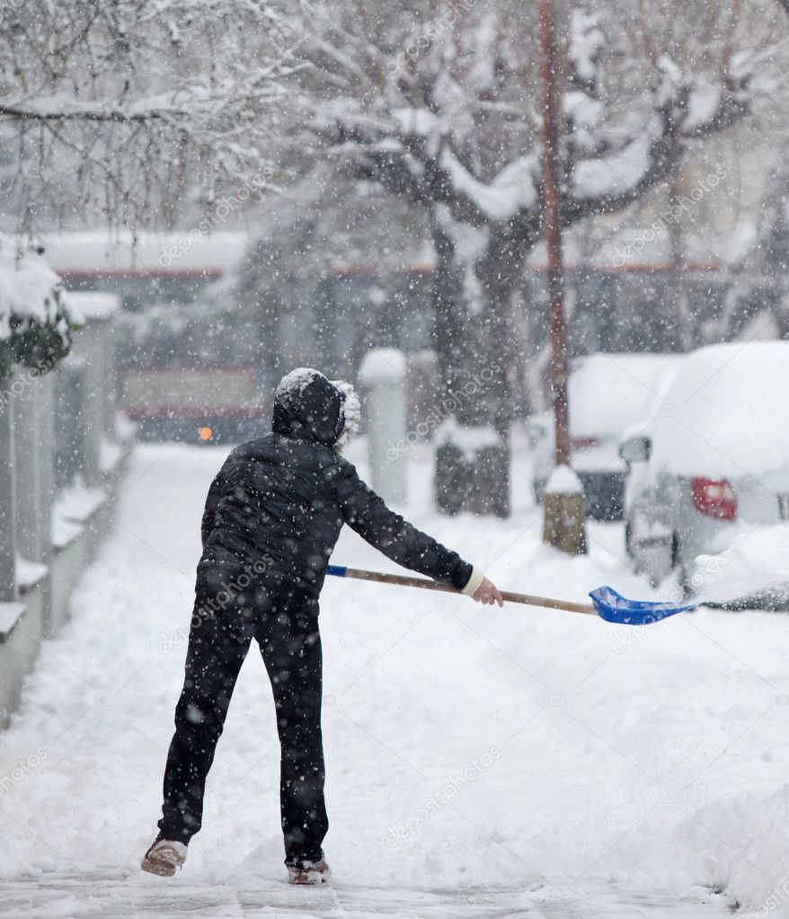 Woman shoveling snow from a sidewalk after a heavy snowfall in a