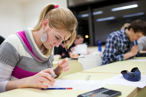 Estudiante universitaria bastante femenina sentado un examen en un salón de clases lleno — Foto de Stock