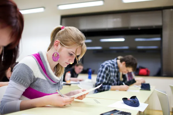 Estudiante universitaria bastante femenina sentado un examen en un salón de clases lleno —  Fotos de Stock