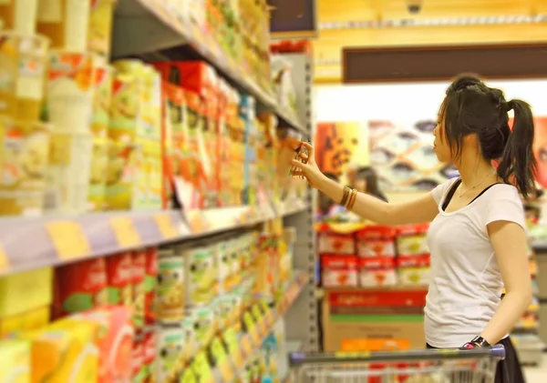 Menina em um supermercado andando no supermercado com um carro de compras — Fotografia de Stock