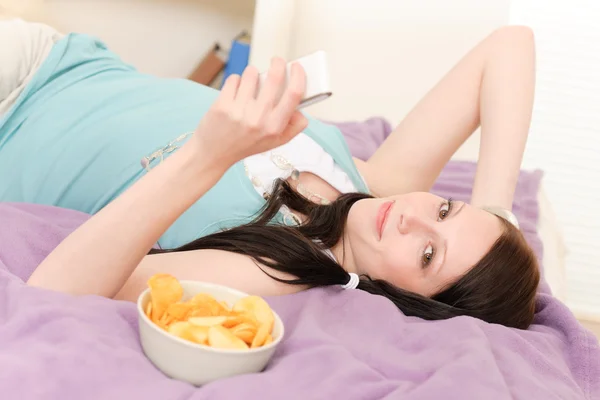 Mladý student, ležící na posteli jíst chipsy — Stock fotografie