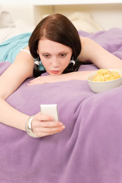 Jonge student meisje op bed houd telefoon — Stockfoto