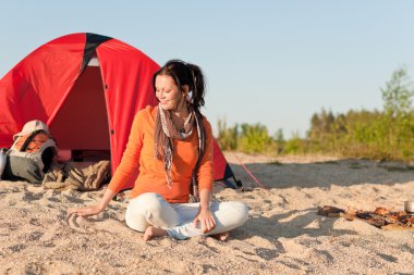 Camping happy woman sitting by campfire on beach clipart