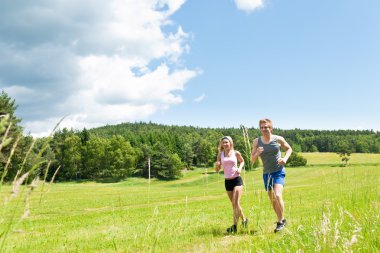 Sportif genç bir çift jogging Meadows güneşli yaz