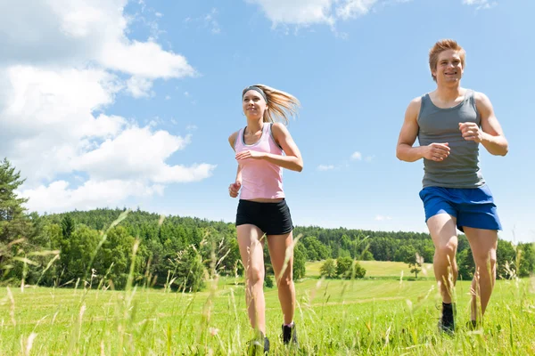 Спортивная молодая пара бегает по лугам солнечным летом — стоковое фото