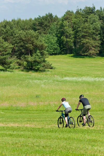 Esporte montanha casal ciclismo downhill ensolarado prados — Fotografia de Stock
